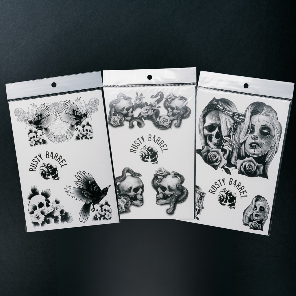 Three temporary tattoos with black and white designs, including skulls and flowers, displayed on paper transfers.