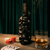 Skull-shaped bottle of Rusty Barrel Caribbean Gold Rum with a glass of whiskey on a table with playing cards and poker chips.