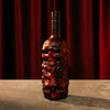 Skull-shaped Rusty Barrel Spiced Rum bottle with intricate designs on a dark surface with red curtain background