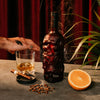 Skull-themed Rusty Barrel Spiced Rum with a glass of whiskey, orange, and smoking plant on a dark surface.