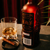 Bottle of Rusty Barrel Spiced Rum with a glass of rum and a cigar on a table.