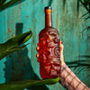 Hand holding a red skull-shaped bottle against a textured blue background