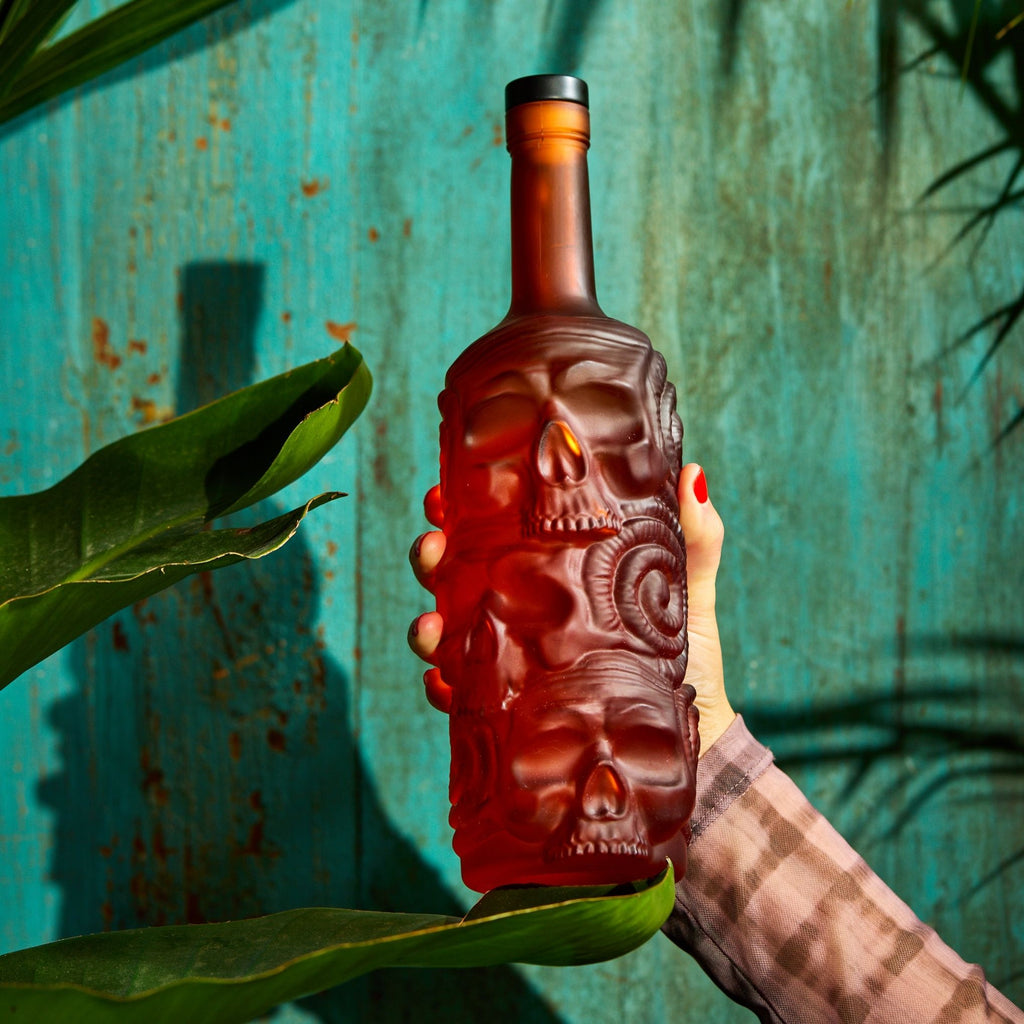 Hand holding a red skull-shaped bottle against a textured blue background