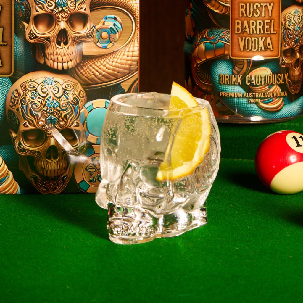 Glass skull with lemon slice on a pool table with Rusty Barrel Vodka bottle and skull decorations.