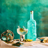 Blue bottle of Rusty Barrel London Dry Gin with a cocktail and lime on a textured teal background
