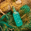 Blue glass bottle of Rusty Barrel London Dry Gin on a textured surface with fishing net and stones