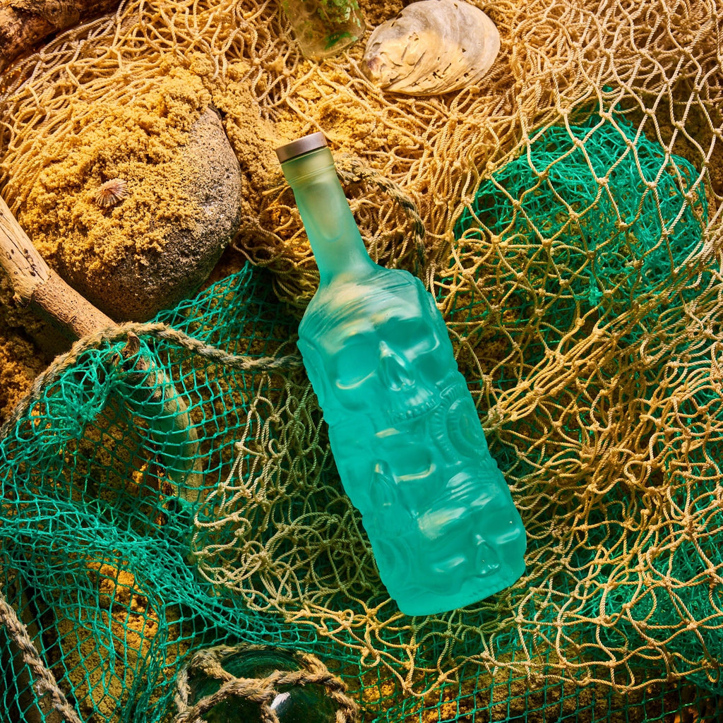 Blue glass bottle of Rusty Barrel London Dry Gin on a textured surface with fishing net and stones