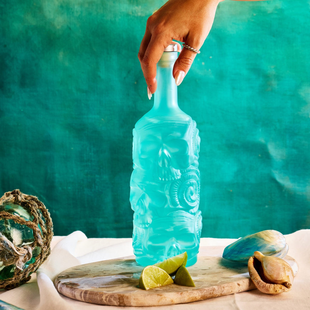 Blue bottle of Rusty Barrel London Dry Gin with decorative design held by a hand against a teal background