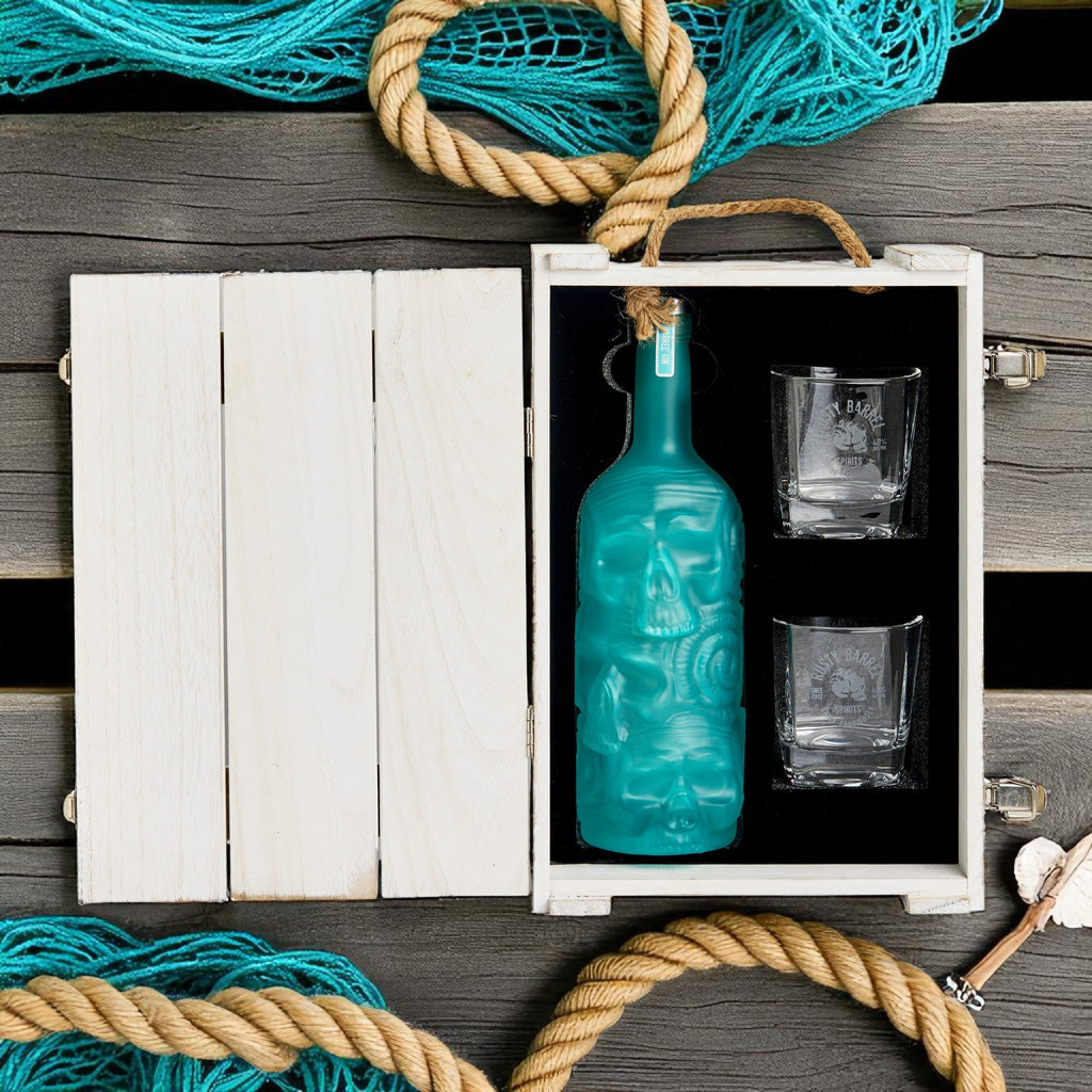 Rusty Barrel London Dry Gin Teal bottle and glasses in a white wooden box with fishing net and rope on a wooden surface