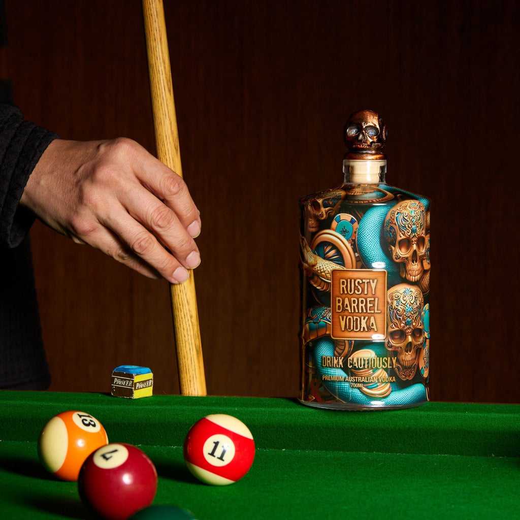 Bottle of Rusty Barrel Vodka on a pool table with pool cues and balls.