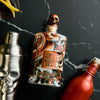 Bottle of Rusty Barrel Vodka with skull design on a dark surface with cocktail shaker and bottle.