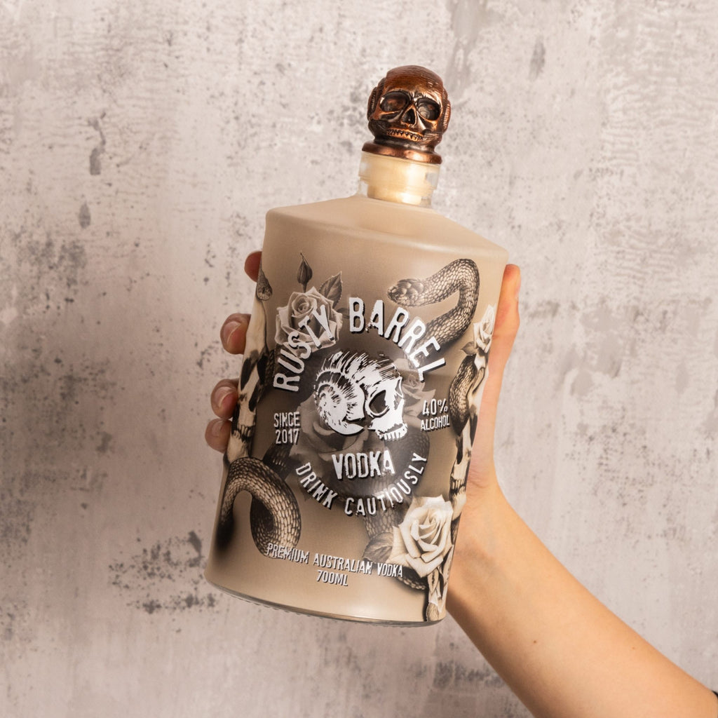 Bottle of Rusty Barrel Vodka 700ml Bondi Ink  held by a hand against a textured gray background