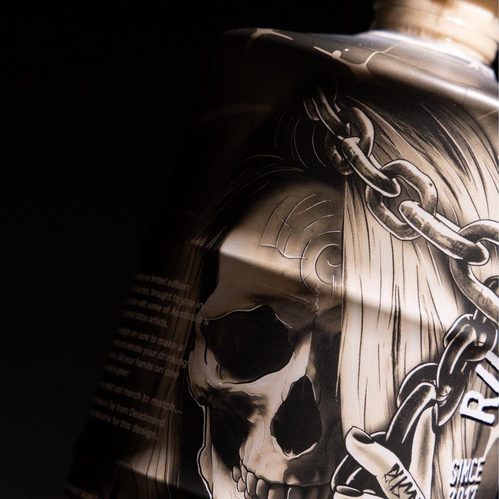 Close-up of a tattoo design by Deadmind Tattoo on a featuring a skull and chain on a 700ml Rusty Barrel Vodka bottle on dark background.