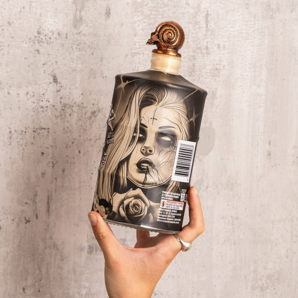 Bottle or Rusty Barrel Vodka 700ml Deadmind Tattoo with artistic label held by a hand against a textured gray background
