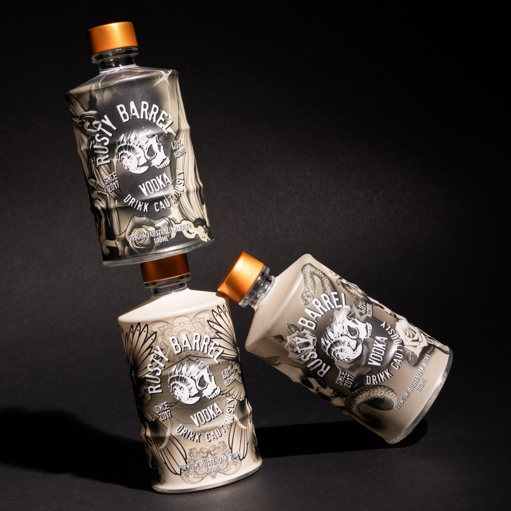 Three Rusty Barrel Vodka 100ml tattoo series bottles on a black background